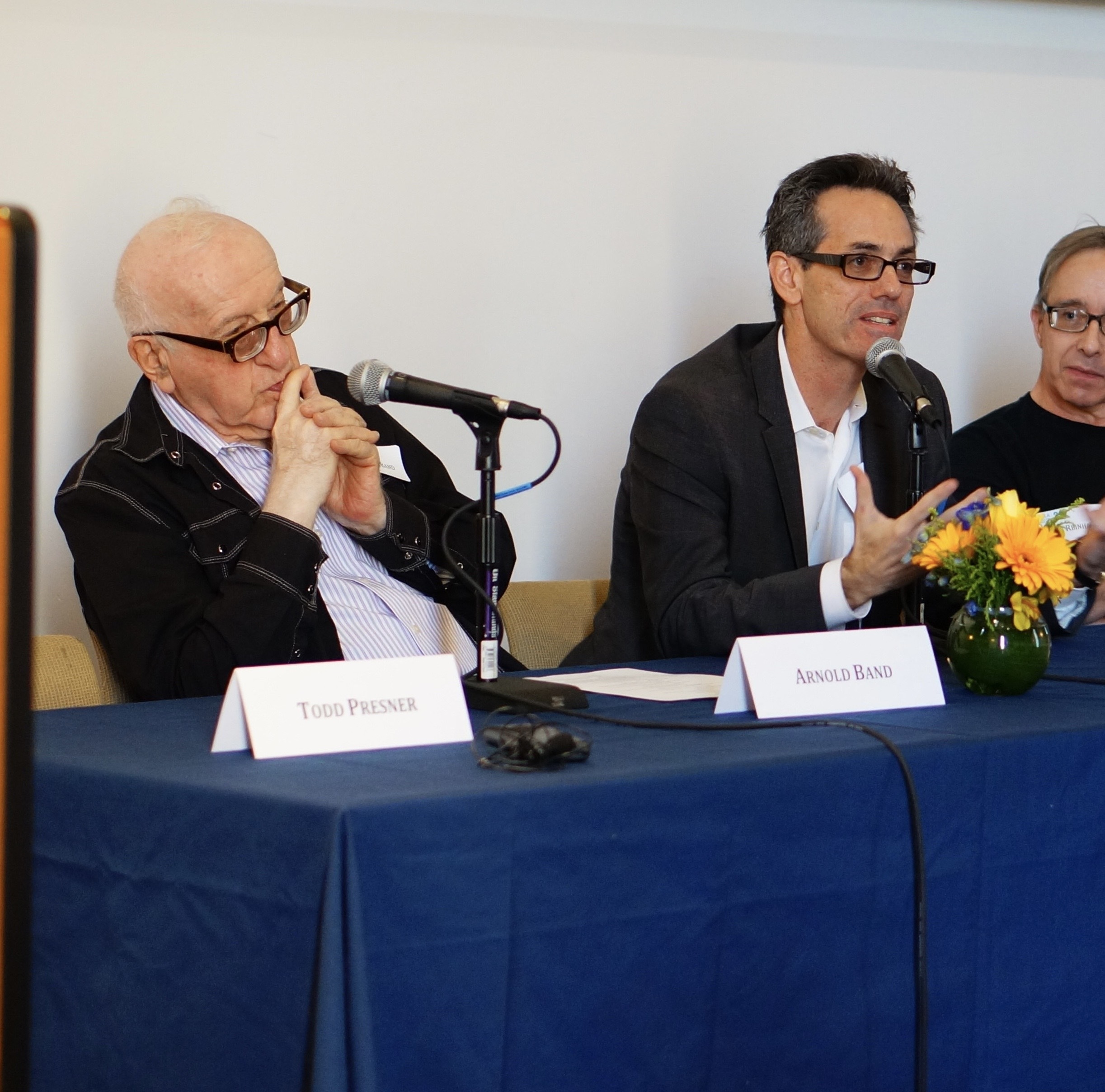 Two men sit together on a panel while a third looks on.