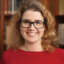 Headshot photograph of white woman with wavy shoulder-length hair and rectangular glasses.