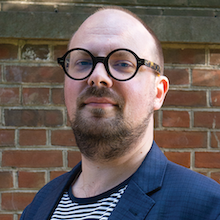 Headshot photograph of white man wearing round glasses.