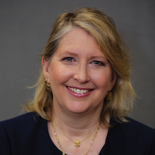 Headshot photograph of white woman wearing gold jewelry.