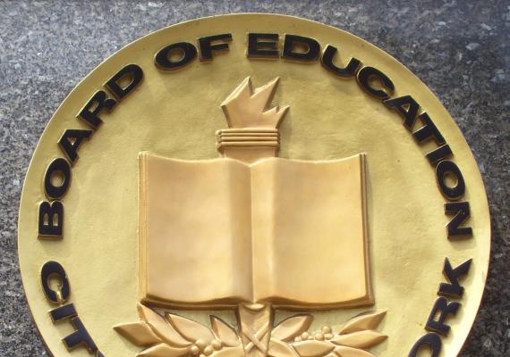 Golden seal with relief of book, torch, and leaves with black lettering reading "board of education city of New York"