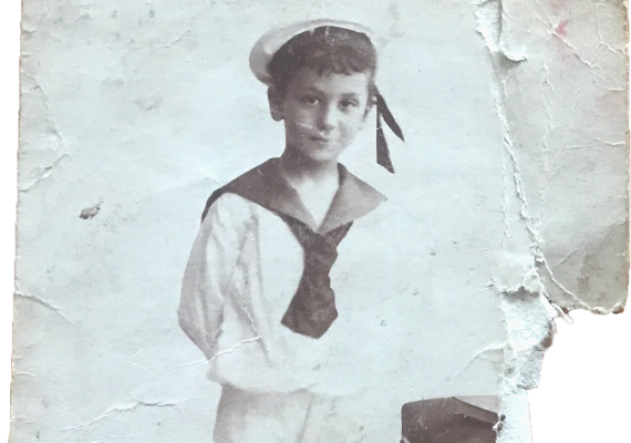 A wrinkled and worn photograph of a young boy wearing a sailor outfit.