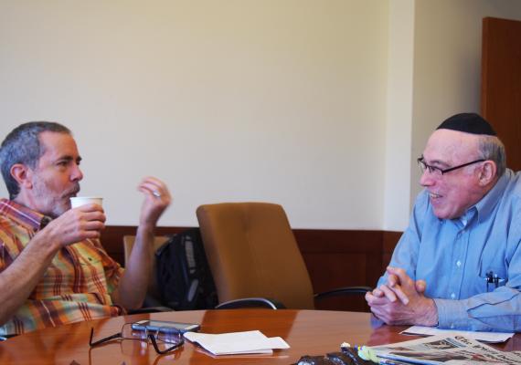 two men sit, talking and laughing at a table