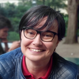 Woman with short hair and glasses seated outdoors.