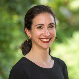 Woman with hair pulled into low ponytail wears hoops and a dark shirt.