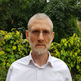 Older man stands in front of foliage.