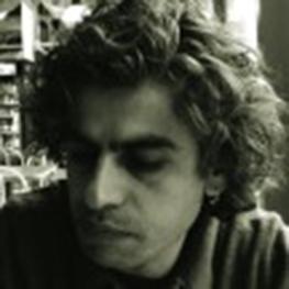 Moody, black and white photograph of seated man looking down and to his right.