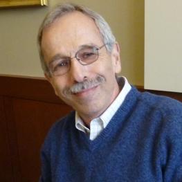 A smiling man wearing glasses leans to his right.